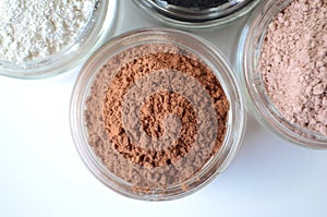A closeup of cosmetic clays for detox face masks - French green clay, kaolin, pink clay, red clay and powdered activated charcoal
