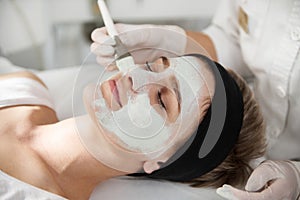 Closeup of cosmetologist applying an alginic mask on a beautiful woman face