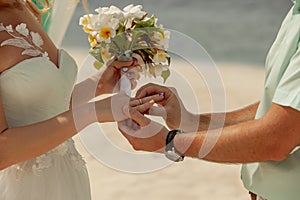 Closeup of a couple exchanging wedding rings during a wedding ceremony on the beach