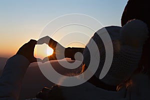 Closeup of couple making heart shape with hands and sunrise background, Couple in love, Focus on hands, Man and woman tourists in
