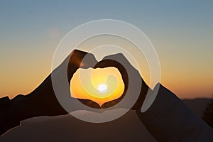 Closeup of couple making heart shape with hands and sunrise background, Happy in love