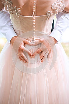 Closeup of couple making heart shape with hands. Wedding couple on the nature is hugging each other. Beautiful model girl in white