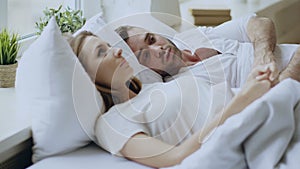 Closeup of couple with relationship problems having emotional conversation while lying in bed at home. Young woman turn