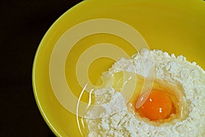 Closeup cracked egg on raw flour in a yellow mixing bowl