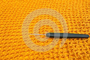 Closeup of crochet hook with black handle lieing on bright yellow crochet net texture