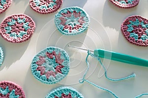 Closeup of crochet tricot hook with chain started, small crochet circle motifs on white surface with bold shadows in hard light,