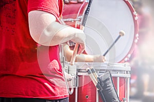 Closeup crop of girl in red tee shirt playing the drums in marching band with blurred drummer behind and lens flare