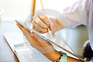 Closeup and crop hands of student studying and make a short note on tablet at school with sun flare background. Network education