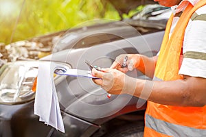 Closeup and crop insurance agent writing on clipboard while examining car after accident claim being assessed and processed