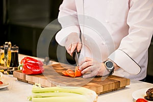 Closeup cropped photo of man cutting tomato on a cutting board in the kitchen