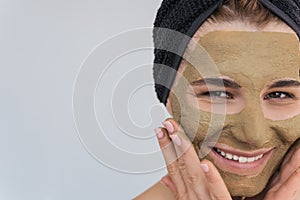 Closeup cropped portrait of beautiful young female doing beauty treatment on her face clean skin with organic clay, looks at the