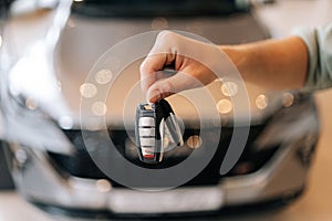 Closeup cropped shot of unrecognizable buyer male holding in hand car key from new auto after buying at showroom on