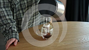 Closeup cropped shot of unrecognizable woman pouring hot water in cup with drip coffee bag. Process of making brewed