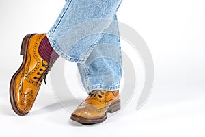 Closeup of Crossed Mens Legs in Brown Oxford Brogue Shoes. Posing in Blue Jeans Against White Background