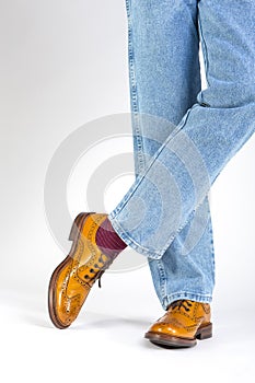 Closeup of Crossed Mens Legs in Brown Oxford Brogue Shoes. Posing in Blue Jeans Against White Background