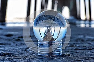 Closeup of a crystal ball reflecting surface on a beach under a fishing pier