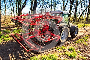 closeup cultivator on soil road against spring trees sky