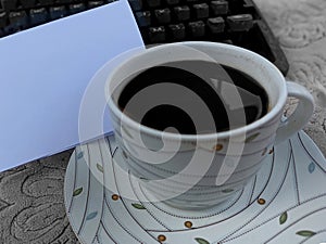 Closeup of a cup of black coffee with blank white notepaper and part of old typewriter keyboard. Copy space for business text.