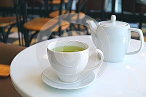 Closeup a cup of green tea with teapot served on a white round table