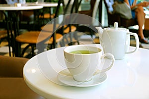 Closeup a cup of green tea and teapot on white round table in a tearoom