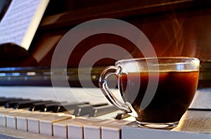 Closeup a Cup of Hot Coffee with Smoke on the Piano with Blurry Music Sheet