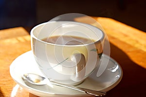Closeup of a cup of hot tea with smoke on mug put on wooden table and bright light in sunshine in afternoon, Traditional english t