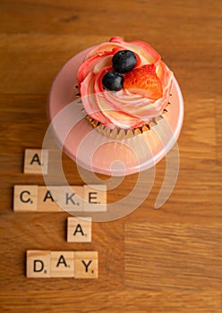 Closeup of cupcake with chocolate frosting and cinder toffee with letters "A cake day" on the table