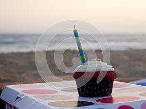 Closeup of a cupcake with stripped candle and blurred background of sand beach