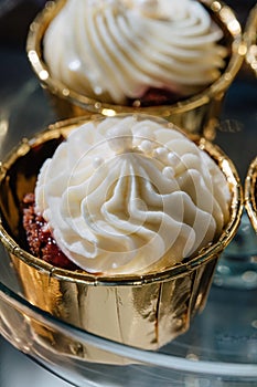 Closeup of cupcakes with cherries in golden cups. Topped with white cream.