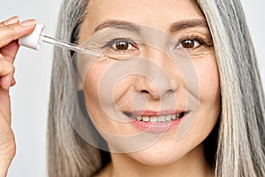 Closeup cut portrait of mature senior Asian woman with pipette serum essence.