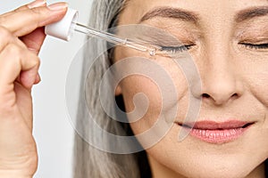 Closeup cut portrait of mature senior Asian woman with pipette serum essence.