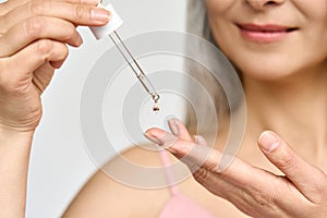 Closeup cut shot of mature Asian woman putting pipette serum essence in hand.