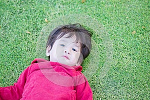 Closeup cute asian kid lie on grass floor in park textured background with copy space