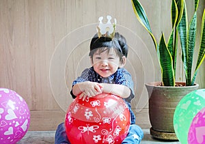 Closeup cute asian kid with paper crown and balloon in birthday party in room textured background with copy space