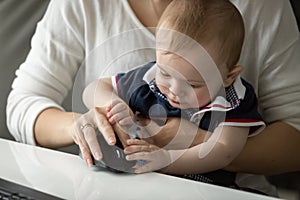 Closeup of cute baby boy sitting on mothers lap and playing with