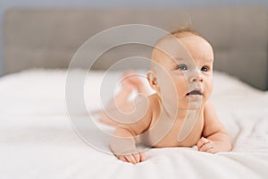 Closeup of cute little baby girl lying on stomach on bed, learning to hold head. Portrait of nice newborn naked baby