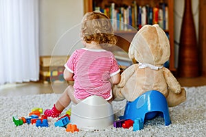 Closeup of cute little 12 months old toddler baby girl child sitting on potty. Kid playing with doll toy. Toilet