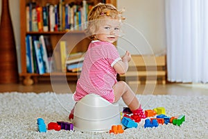 Closeup of cute little 12 months old toddler baby girl child sitting on potty. Kid playing with doll toy. Toilet