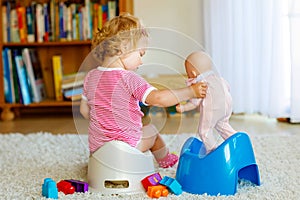 Closeup of cute little 12 months old toddler baby girl child sitting on potty. Kid playing with doll toy. Toilet