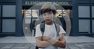 Closeup cute school boy standing with hands crossed. Pupil posing on schoolyard.