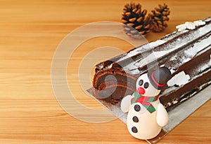 Closeup a Cute Snowman Marzipan of Christmas Roll Cake on Wooden Table with Blurry Dry Pine Cones in Background