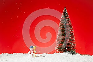 Closeup of a cute snowman toy on fae snow with a Christmas tree on it against a red background