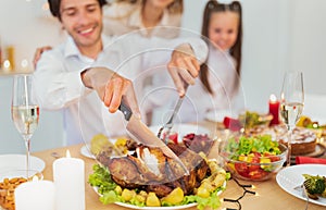 Closeup of dad cutting roasted turkey for Christmas or Thanksgiving, celebrating holiday with wife and daughter at home