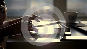 closeup, dark silhouette of female hands. she is typing something in tablet, next is a cup, mobile, laptop on table