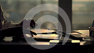 closeup, dark silhouette of female hands. she is typing something in tablet, next is a cup, mobile, laptop on table