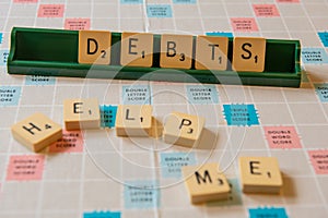Closeup of debts and help me written on a scramble board under the lights