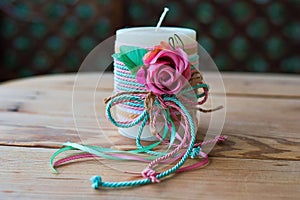 Closeup of a decorative white candle, with a rose and ribbons on a wooden table
