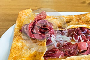 Closeup of delicious crepe with dried meat pastrami served on a white plate
