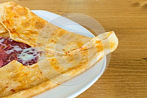 Closeup of delicious crepe with dried meat pastrami served on a white plate