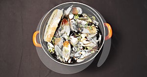 Closeup of delicious mussels in a creamy sauce with red caviar and herbs in a plate. Female hands in gloves taking a bowl